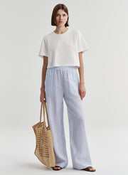 Woman wearing blue striped linen pants with a white top on a plain background