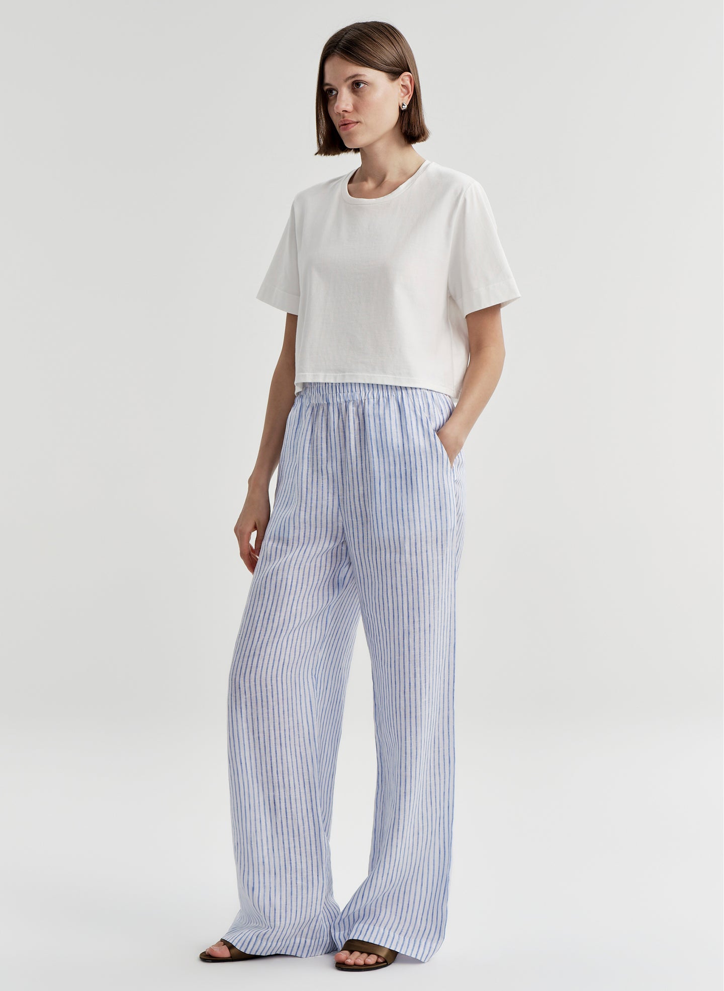 Woman wearing blue striped linen pants with a white top on a plain background