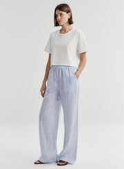 Woman wearing blue striped linen pants with a white top on a plain background