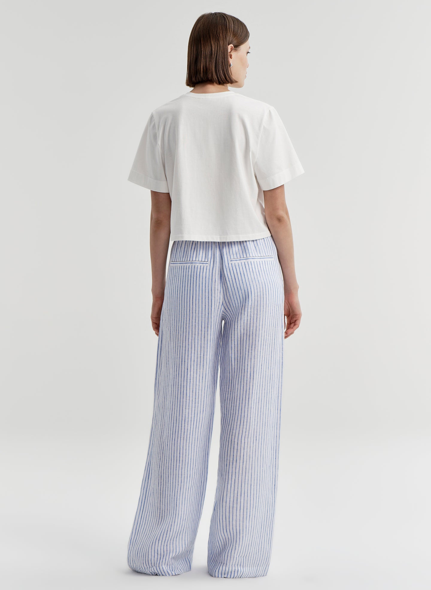 Woman wearing blue striped linen pants with a white top on a plain background
