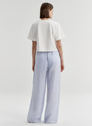 Woman wearing blue striped linen pants with a white top on a plain background