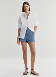 Woman wearing blue linen shorts and a white button up shirt on a light gray background