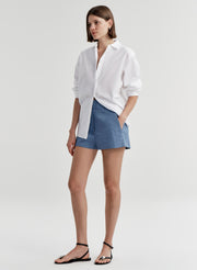 Woman wearing blue linen shorts and a white button up shirt on a light gray background