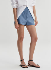 Woman wearing blue linen shorts and a white button up shirt on a light gray background