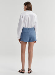 Woman wearing blue linen shorts and a white tucked in shirt on a light gray background