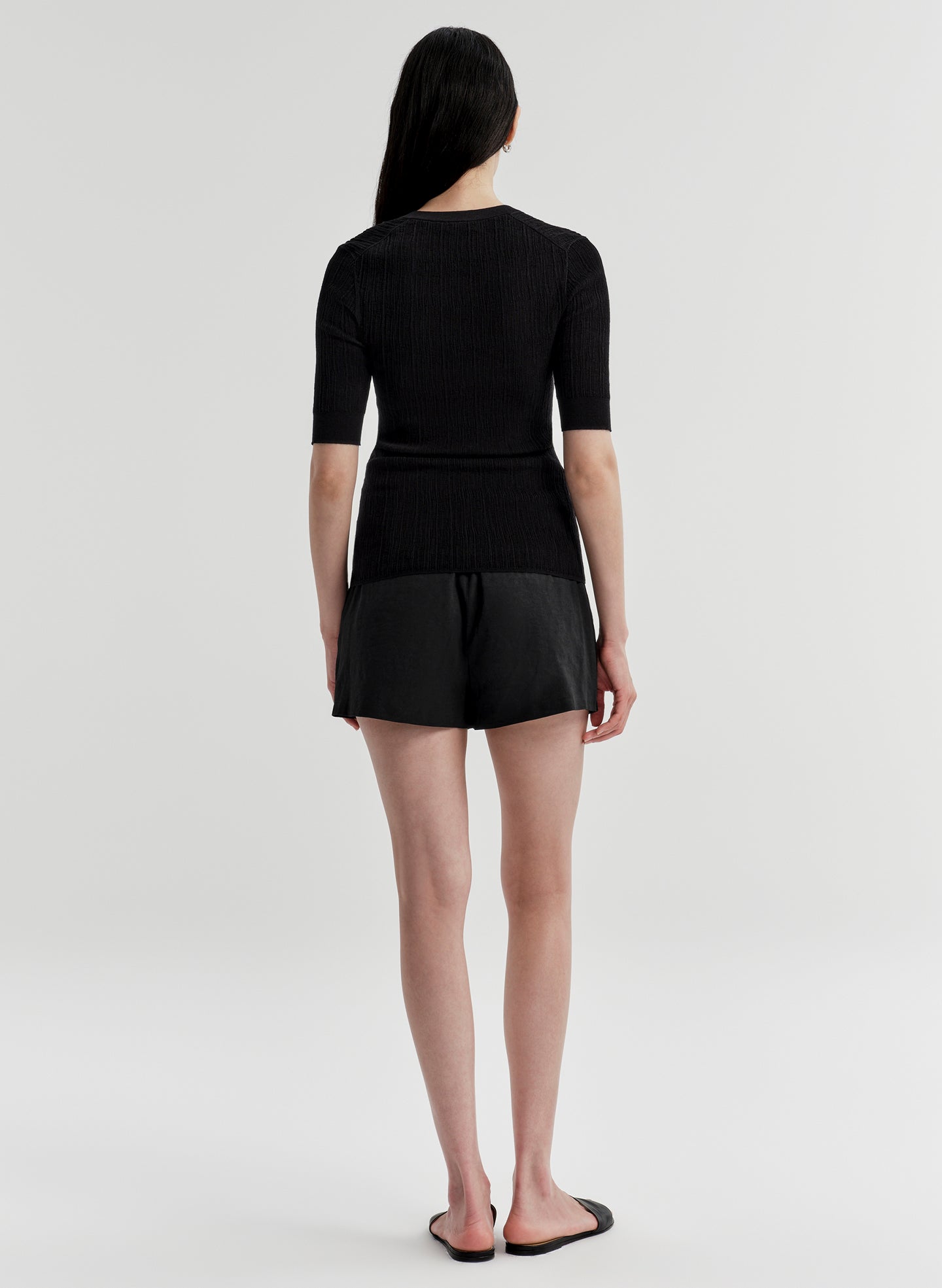 Woman wearing a black top with a black skirt on a plain background