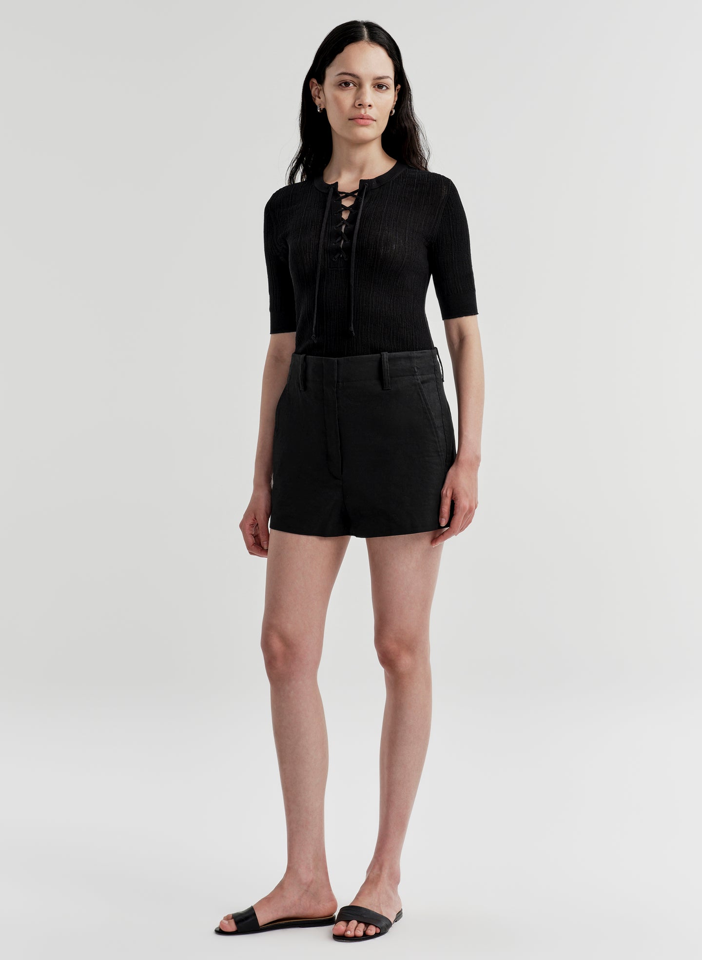 Woman wearing black linen shorts and a black top on a white background