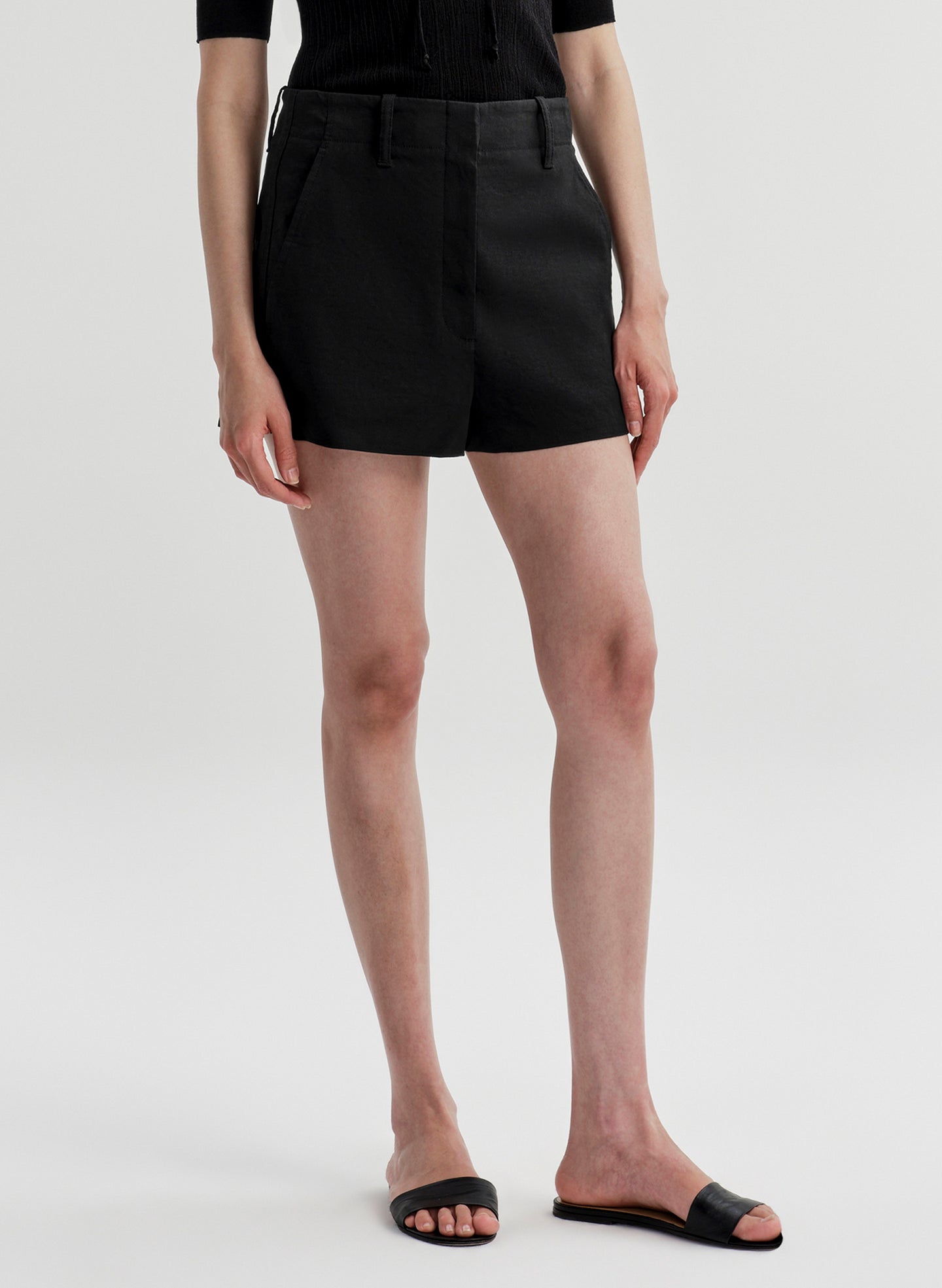 Woman wearing black linen shorts and a black top on a white background