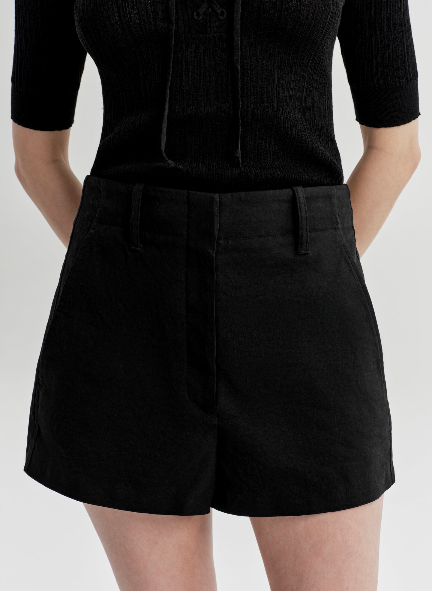 Woman wearing black linen shorts and a black top on a white background
