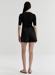 Woman wearing black linen shorts and a black top on a white background
