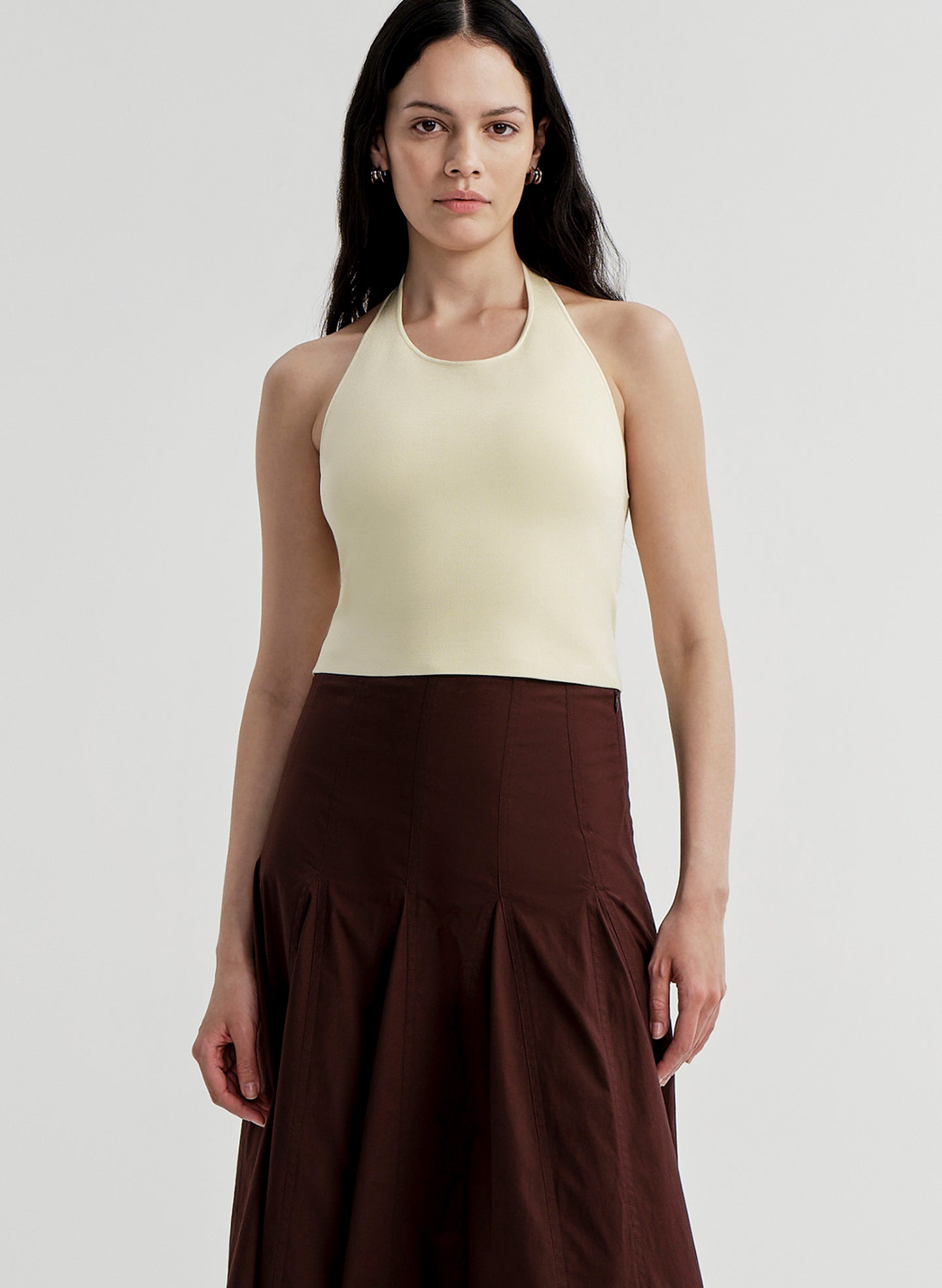 Woman wearing a yellow halter top and brown skirt on a light gray background