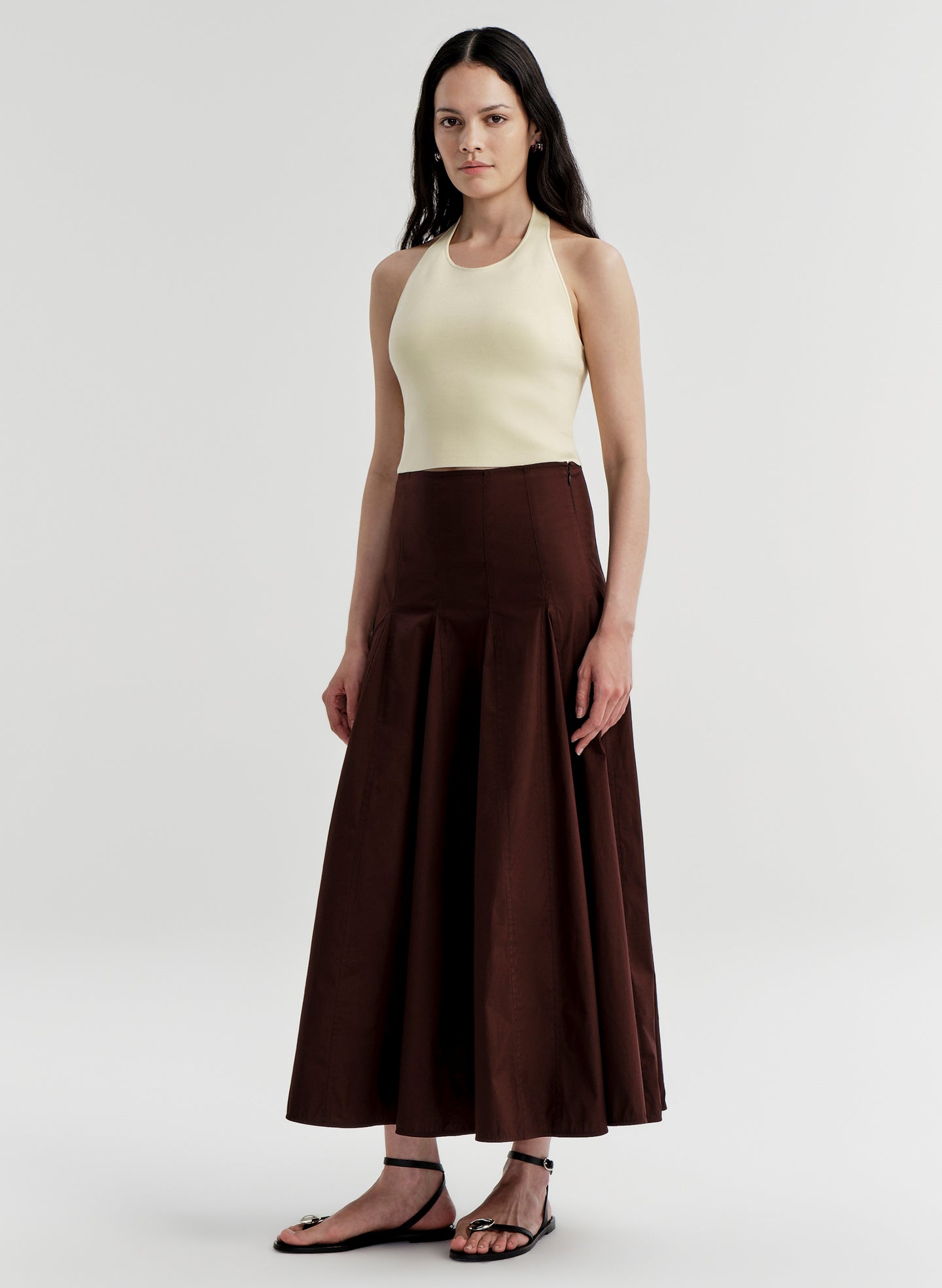 Woman wearing a yellow halter top and brown skirt on a light gray background