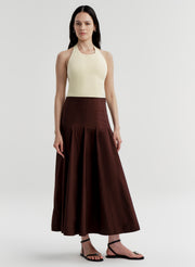 Woman wearing a yellow halter top and brown skirt on a light gray background