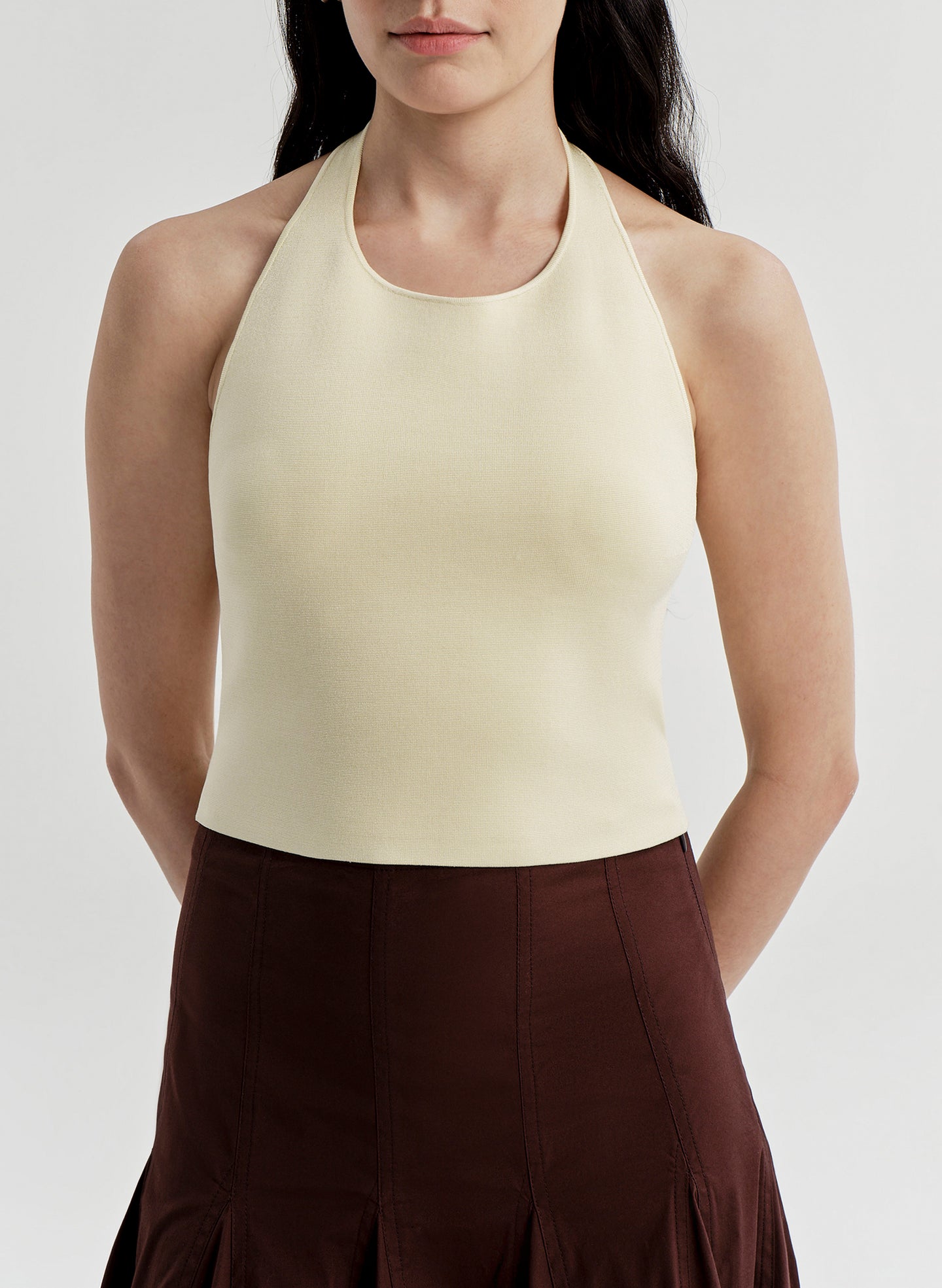 Woman wearing a yellow halter top and brown skirt on a light gray background