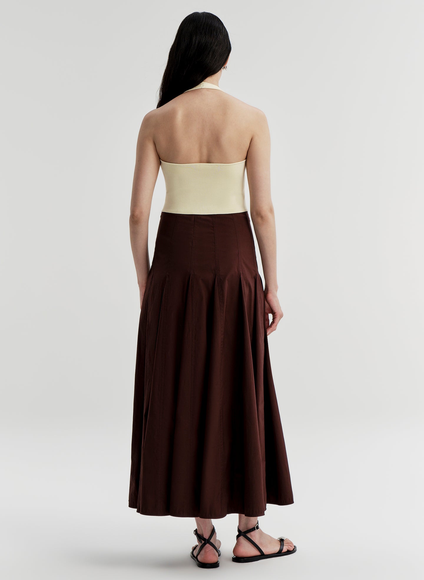 Woman wearing a yellow backless halter top and brown skirt on a light gray background