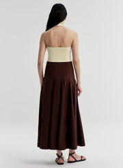 Woman wearing a yellow backless halter top and brown skirt on a light gray background