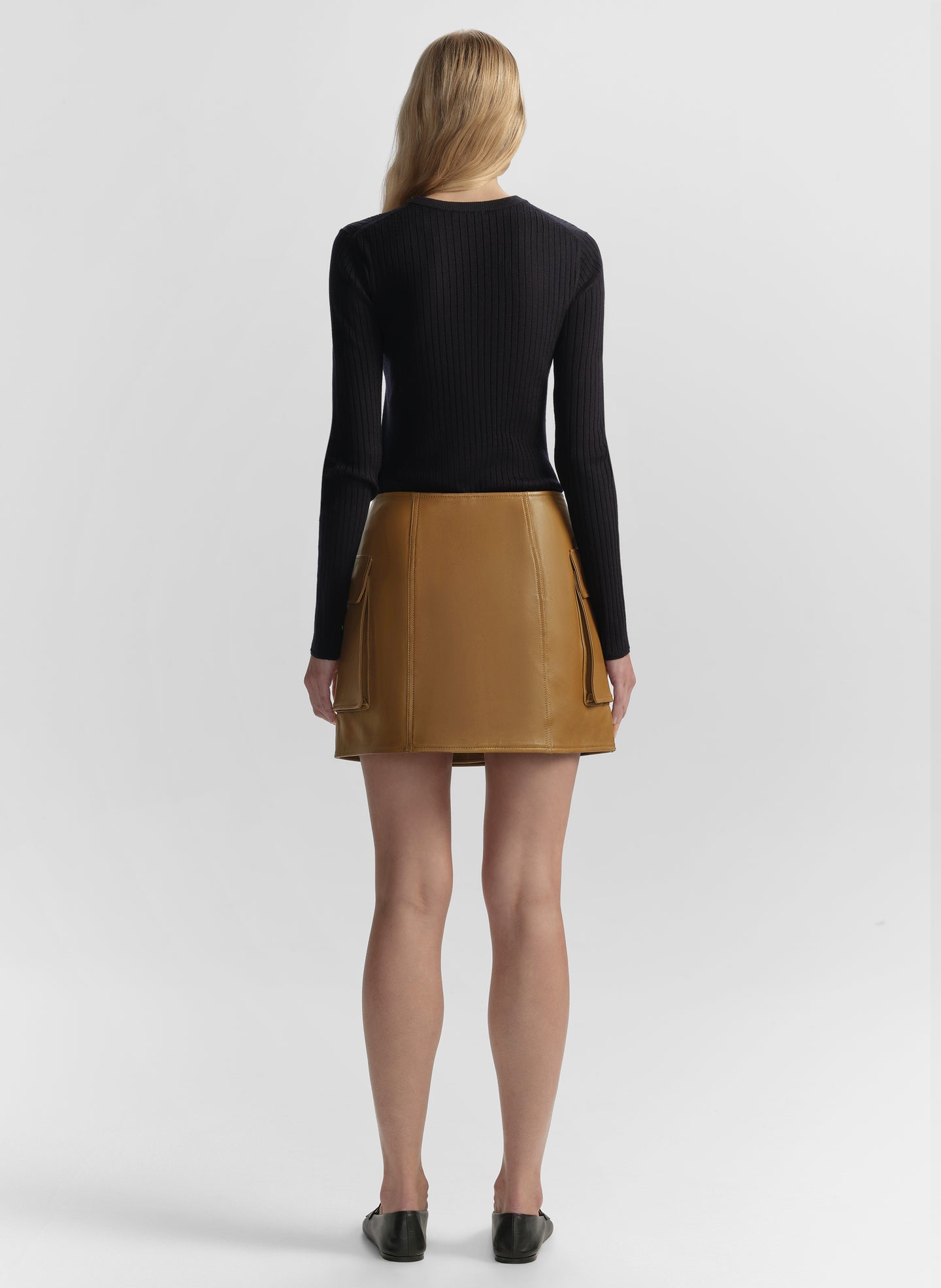 Person wearing a black top and brown leather skirt on a white background