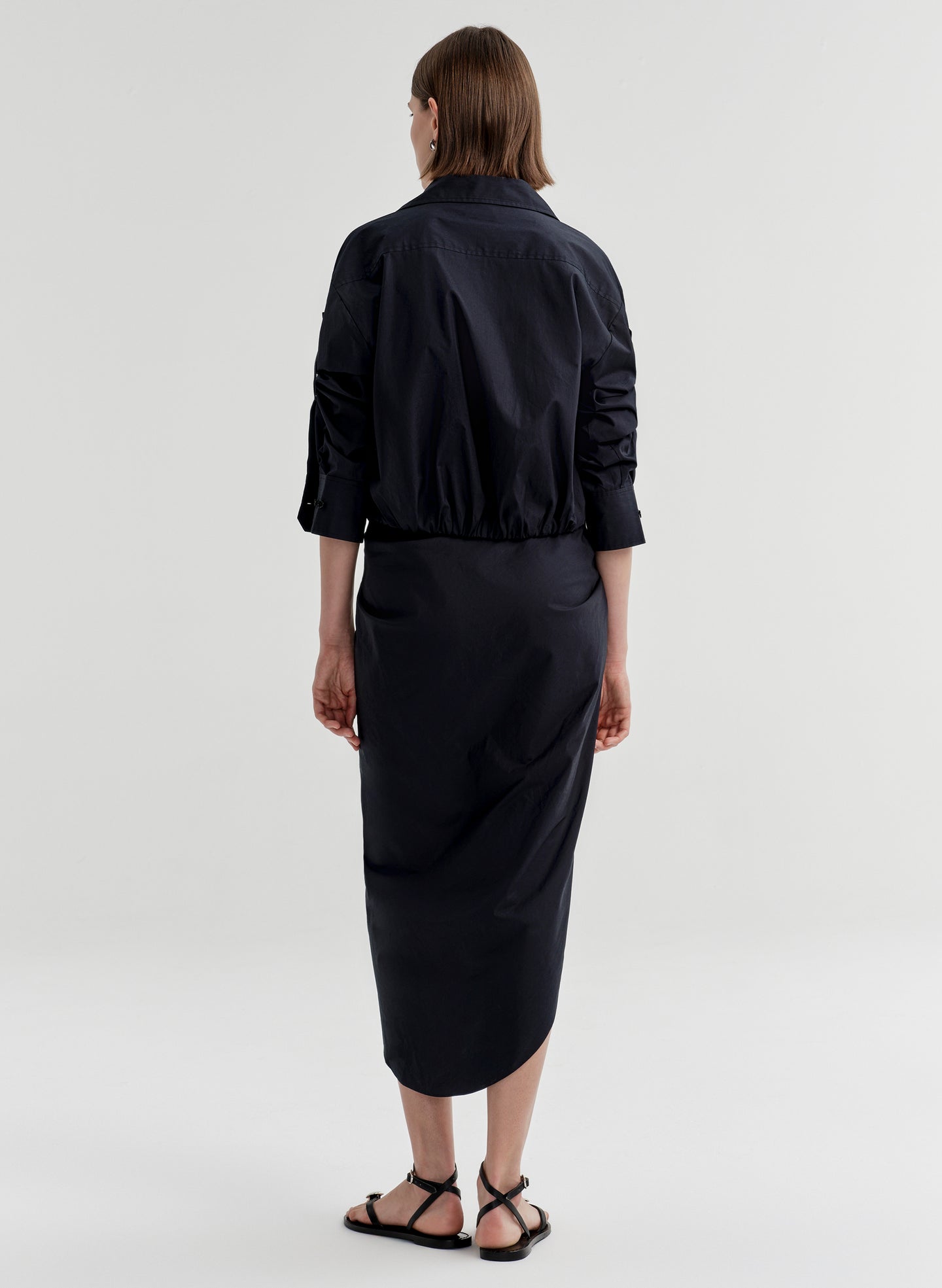 Woman wearing a cropped cotton top with a wide collar and tie waist with a black skirt on a light gray background