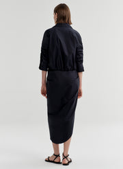 Woman wearing a cropped cotton top with a wide collar and tie waist with a black skirt on a light gray background