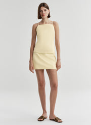 Woman wearing a light yellow top and mini skirt on a white background