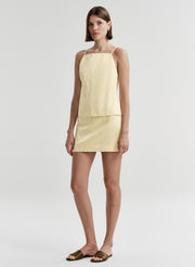 Woman wearing a light yellow sleeveless top and skirt set on a white background