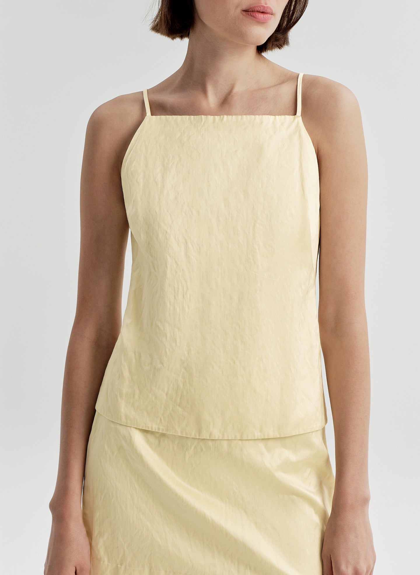 Woman wearing a light yellow sleeveless top against a plain background
