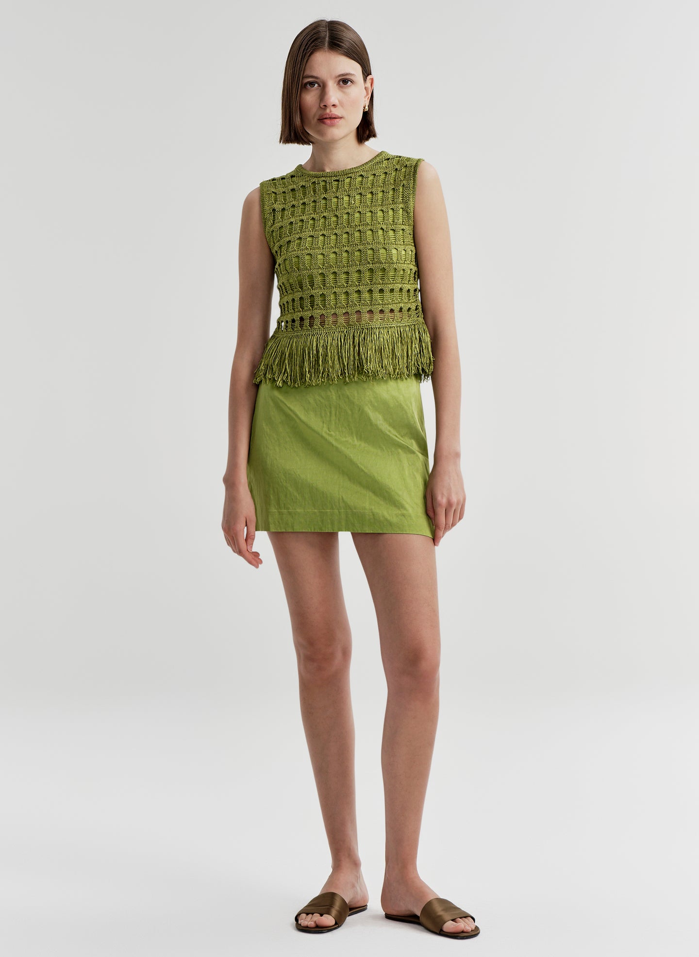 Woman wearing a green sleeveless top and skirt on a white background