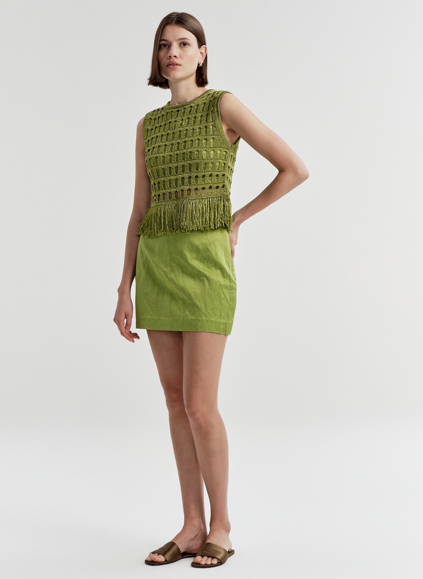 Woman wearing a green sleeveless top and skirt on a white background