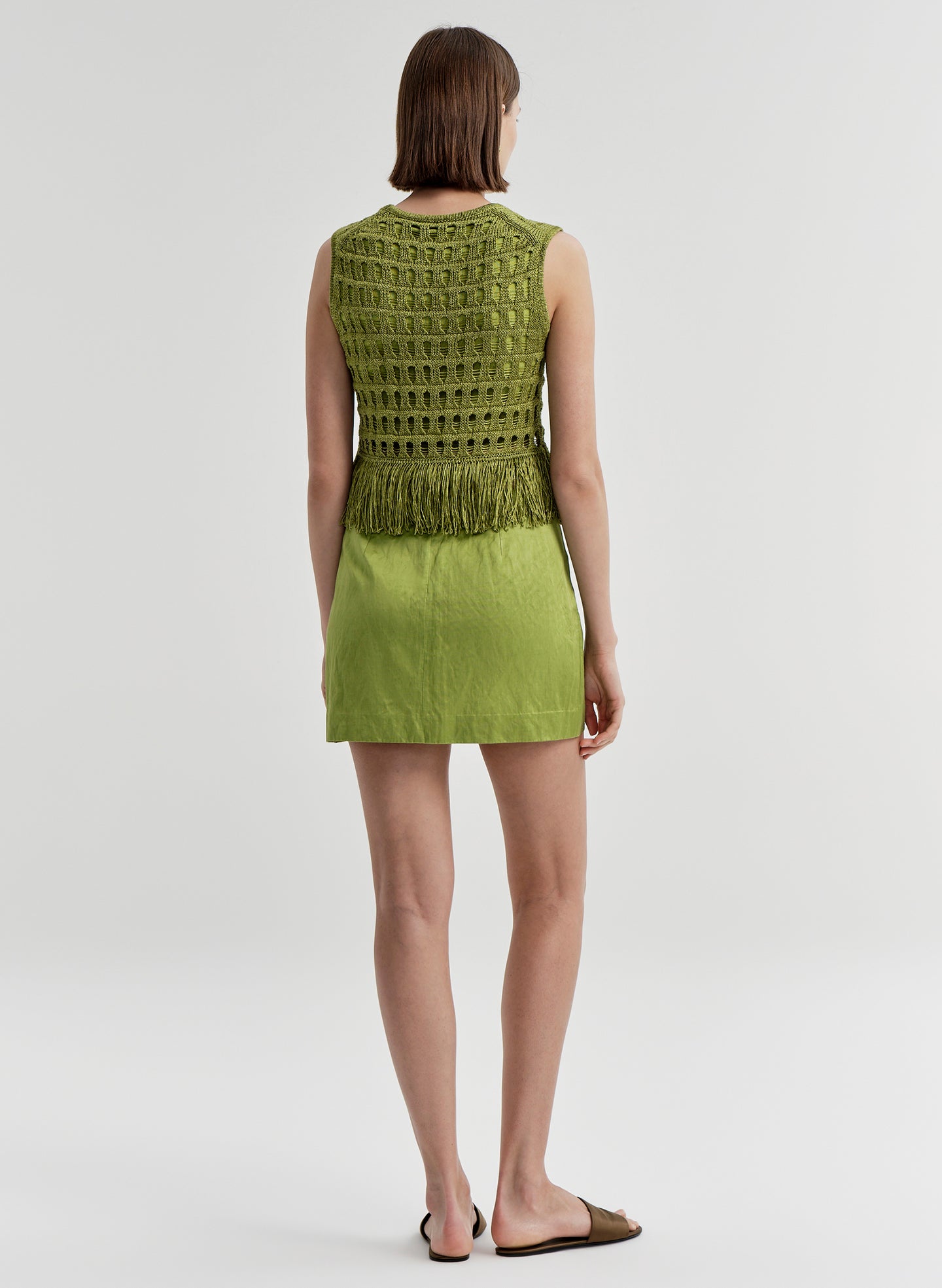 Woman wearing a green crochet top and skirt set on a white background