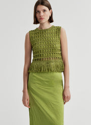 Woman wearing a crochet green sleeveless top with fringe details with a green skirt on a light gray background