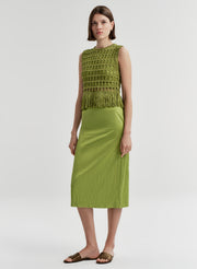 Woman wearing a crochet green sleeveless top with fringe details with a green skirt on a light gray background