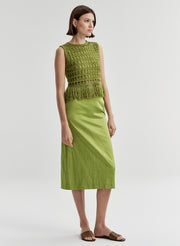 Woman wearing a crochet green sleeveless top with fringe details with a green skirt on a light gray background