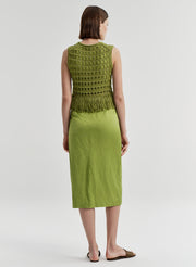 Woman wearing a crochet green sleeveless top with fringe details with a green skirt on a light gray background