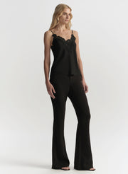 Woman wearing a black lace top and black pants on a white background