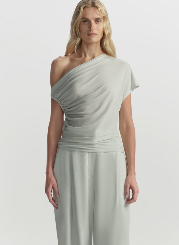 Woman wearing a light green one-shoulder top on a white background