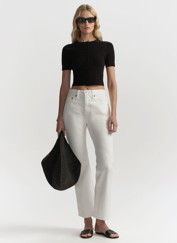 Woman wearing a black top and white pants holding a black bag on a white background