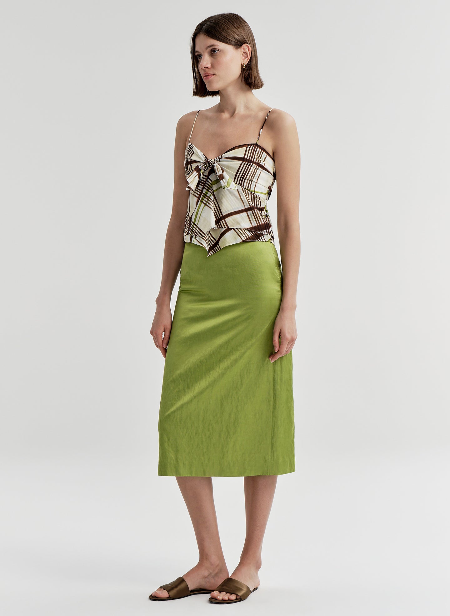 Woman wearing a patterned brown top and green skirt on a plain background