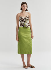 Woman wearing a patterned brown top and green skirt on a plain background