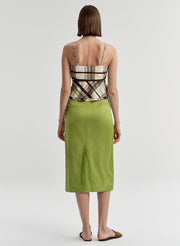 Woman wearing a patterned brown top and green skirt on a plain background