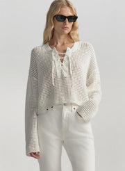 Woman wearing a white textured top and pants with sunglasses on a light gray background