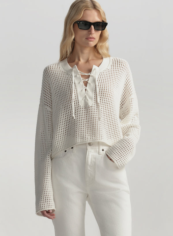 Woman wearing a white textured top and pants with sunglasses on a light gray background