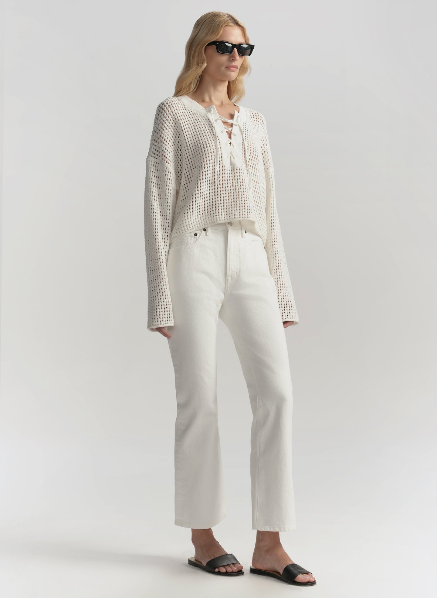 Woman wearing a white outfit with sunglasses on a plain background