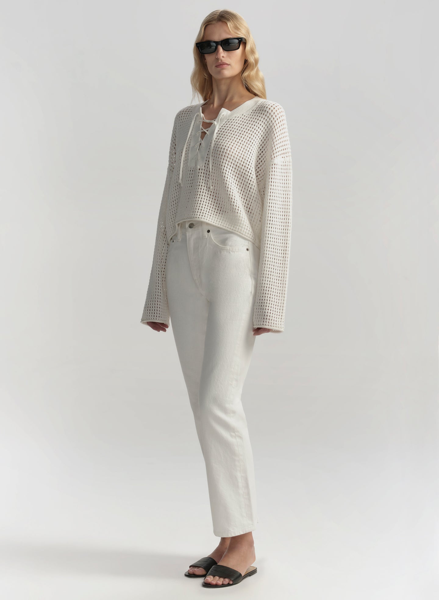 Woman wearing a white outfit with sunglasses on a plain background