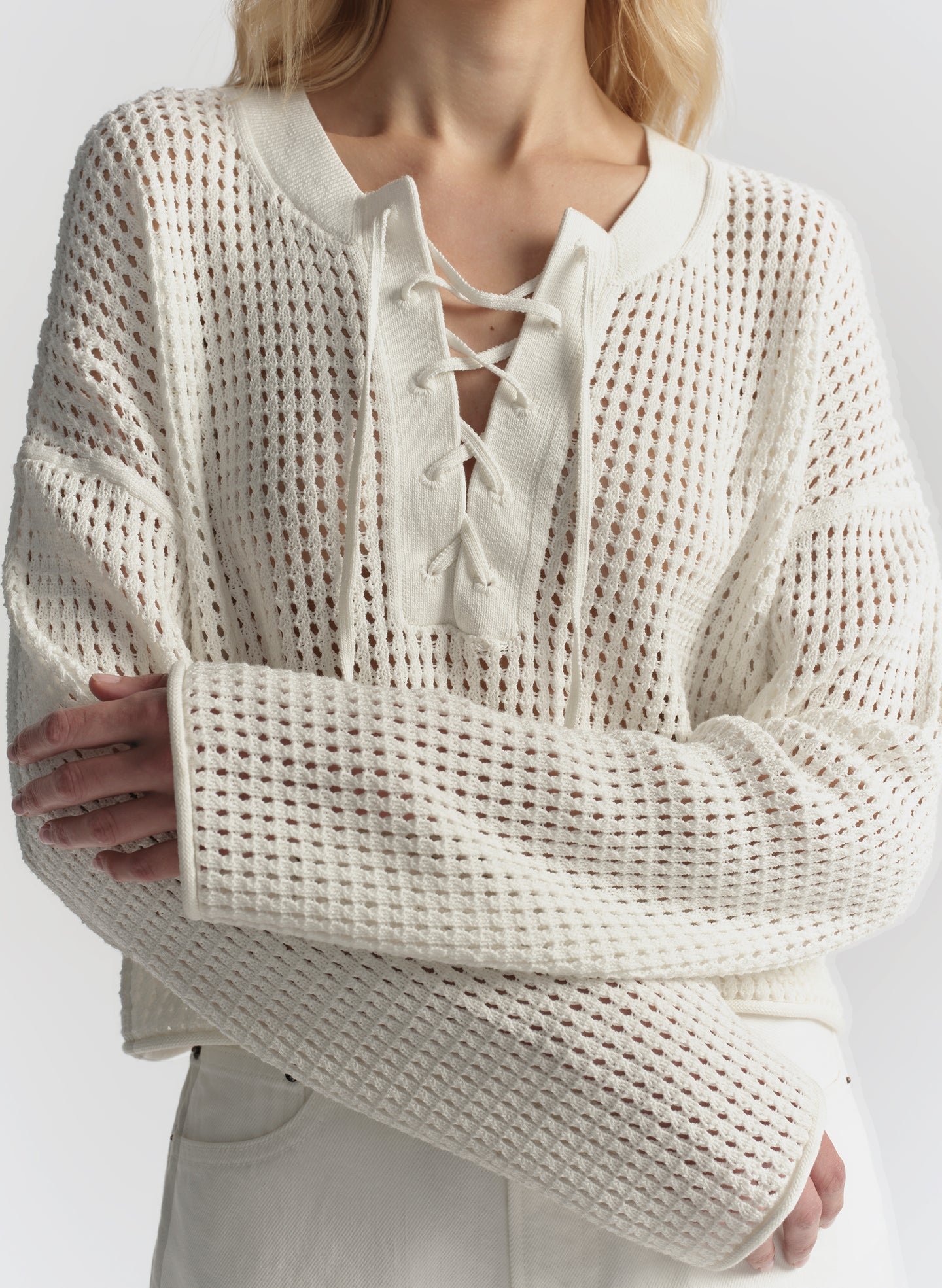 Person wearing a cream-colored knit sweater with lace-up front design on a plain background