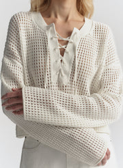Person wearing a cream-colored knit sweater with lace-up front design on a plain background