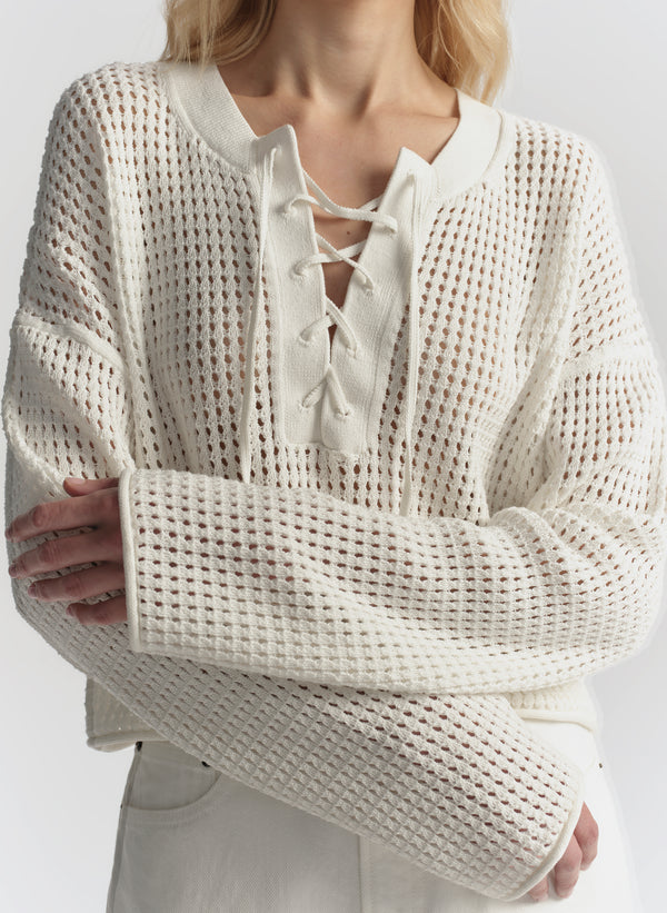 Person wearing a cream-colored knit sweater with lace-up front design on a plain background