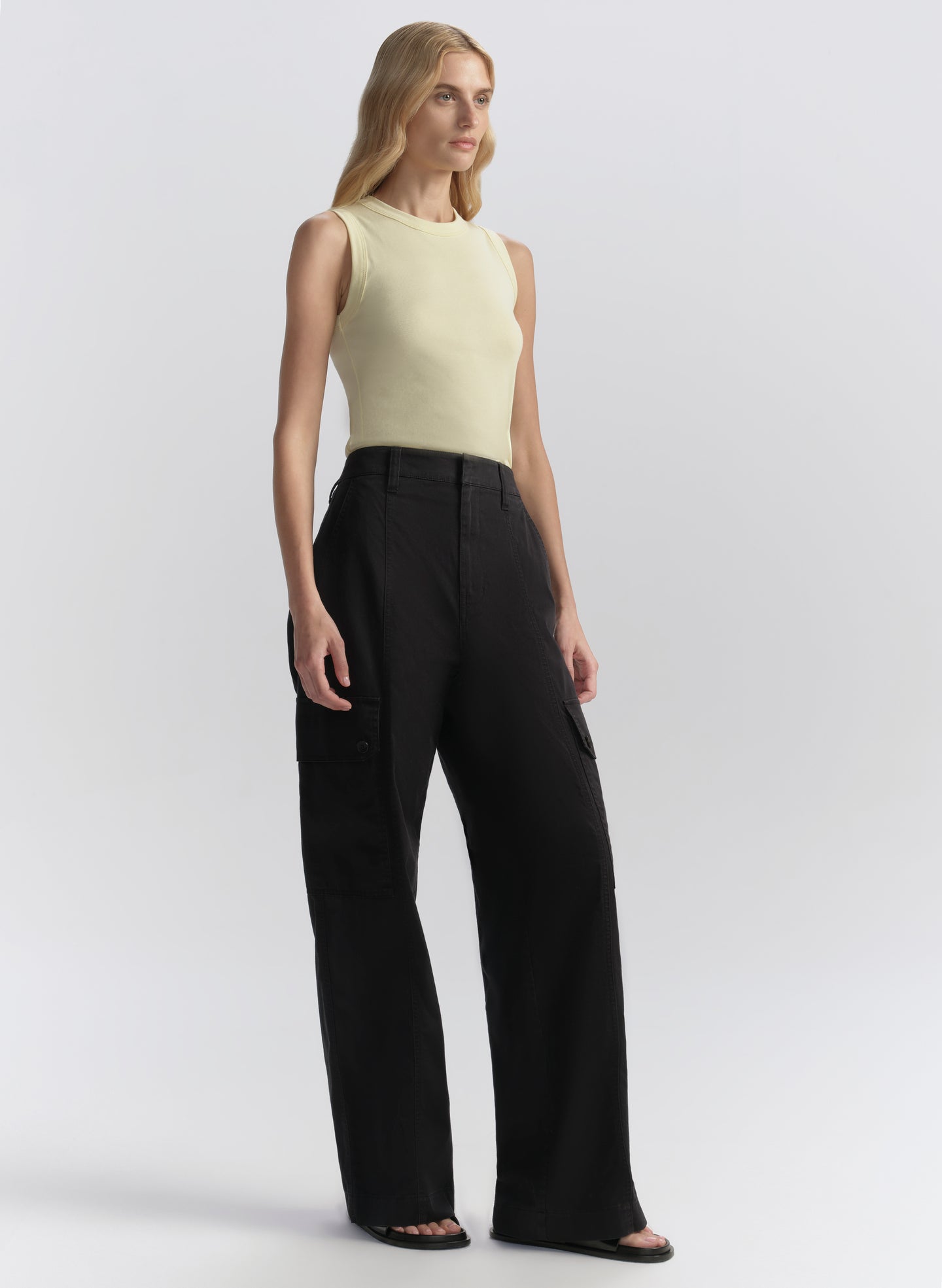 Woman wearing a light yellow sleeveless top and blue pants on a white background