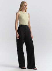 Woman wearing a light yellow sleeveless top and blue pants on a white background