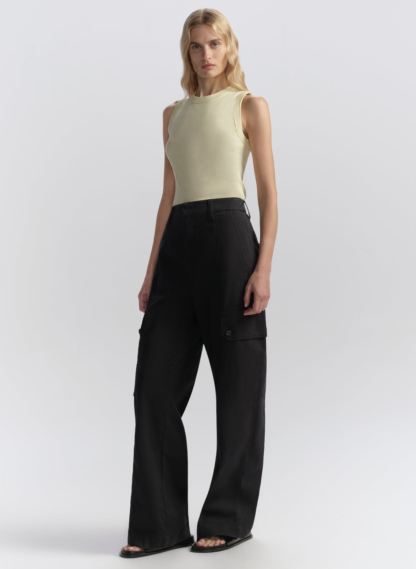 Woman wearing a light yellow sleeveless top and blue pants on a white background