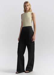 Woman wearing a light yellow sleeveless top and blue pants on a white background